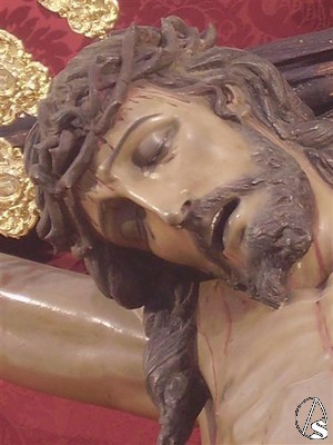 El rostro de Cristo muestra los ojos cerrados y la boca entreabierta, teniendo ladeada su cabeza hacia el lado derecho con la corona de espinas realizada en la misma talla 